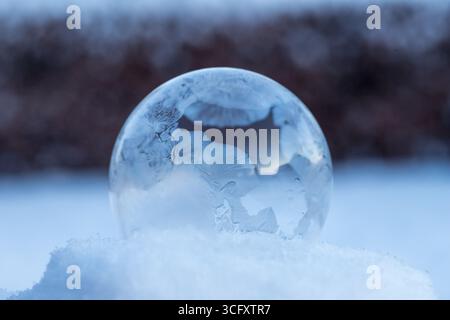 Gefrorene Seifenblase auf Schnee, Winterzauber der gefrorenen Seifenblase mit schönen Eiskristallen in perfekter Kugel auf Schnee mit verschwommenem Hintergrund Stockfoto