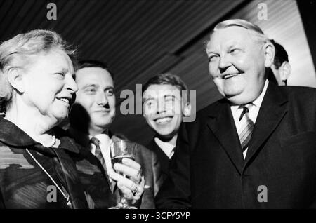 Ludwig Erhard und seine Ehefrau Luise Erhard stehen gemeinsam mit mehreren jüngeren Männern bei einem festlichen Anlass. Beide lachen, Luise Erhard hält ein Glas in der Hand. Stockfoto
