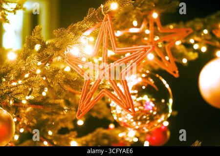Warm leuchtender Weihnachtsbaum mit goldenen Feenlichtern, festlichen Sternornamenten und glänzenden Kugeln. Glitzernde Magie der Winterabende in festlicher Dekoration Stockfoto