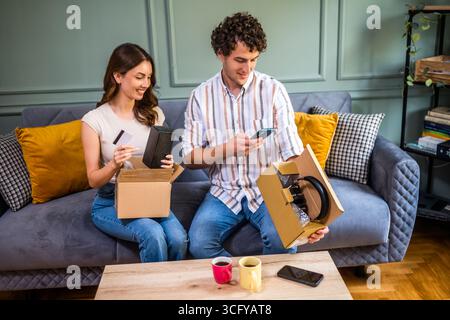 Ein erwachsenes Paar packt ihre Pakete aus, die an die Heimatadresse geliefert werden. Man scannt den QR-Code auf der Verpackung. Stockfoto