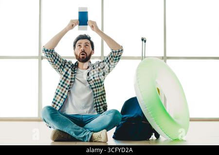Junger Mann am Flughafen mit Reisepass, der sich auf den Urlaub mit Freizeit-Vibes und ungezwungenem Stil vorbereitet Stockfoto