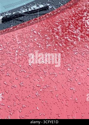 Gefrorene Eiskristalle auf roter Autooberfläche erzeugen winterlichen abstrakten Hintergrund. Mobiles Foto Stockfoto