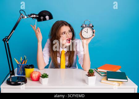 Frustrierter Student mit Wecker in farbenfroher Studieneinrichtung vor blauem Hintergrund Stockfoto