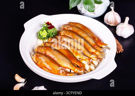 Gebackener gelber Croaker mit Knoblauch im Auflauf auf schwarzem Hintergrund Stockfoto