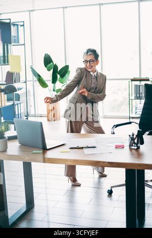 Energiegeladene Geschäftsfrau tanzt in ihrem Büro, während sie formelle Kleidung trägt Stockfoto