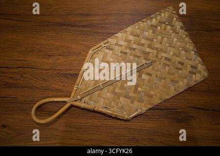 Ein traditioneller, gewebter Bambus-Handventilator auf dem Holztisch. Stockfoto