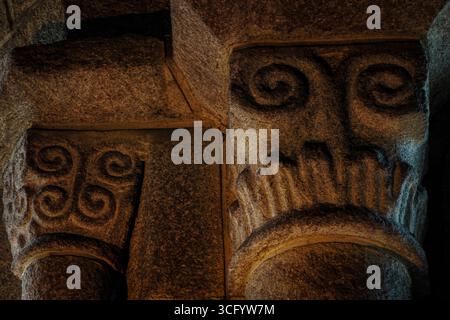 Doppelrollen oder Spiralen in Granitkapitellen in der Kirche Saint Tudy in Loctudy, Finistère, Südwestbretagne, Frankreich, sehen auf den ersten Blick wie Blicke, die auf Besucher herabblicken. Die Kirche aus dem 11. Und 12. Jahrhundert hat mehr als 70 romanische Kapitelle und ihre Säulenbasen gehören zu den reichsten in der Bretagne. Stockfoto