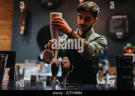 Ein männlicher Barkeeper bereitet in einer Bar zwei Cocktails mit Creme-Belag zu Stockfoto