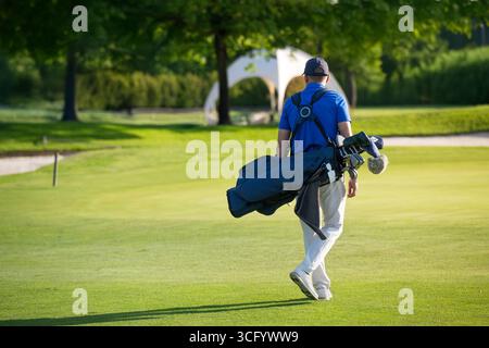 An einem sonnigen Tag läuft der Golfer mit seiner Golftasche auf dem Golfplatz Stockfoto