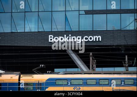 Amsterdam Niederlande 23. August 2025 Booking.com Niederlassungen. Unterhalb eines Zuges der Nederlands Spoorwegen NS-Pässe. Booking.com ist eine Hotelbuchungsplattform. Buchung, hauptsitz, hauptsitz, Logo, Kantoor Stockfoto