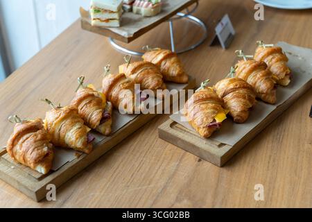 Frisch gebackene Croissants mit Schinken und Käse auf rustikalem Holzbrett, Teil eines Frühstücks- oder Brunch-Buffets. Stockfoto