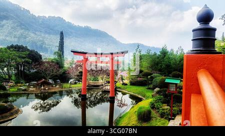 Japanisches rotes Torii-Tor neben dem See mit wunderschönen Hügeln und blauem Himmel Stockfoto