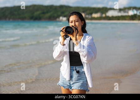 Eine leidenschaftliche Reisende und Fotografin genießt einen freudigen Moment am Meer und fängt mit ihr die Schönheit des Strandes und das Licht der goldenen Stunde ein Stockfoto