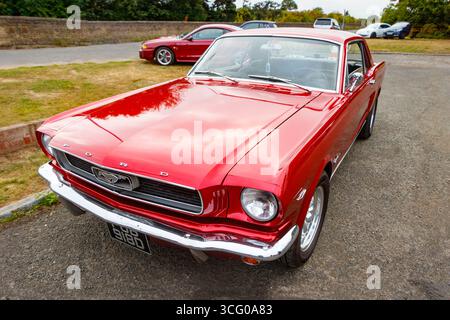 Klassischer roter Ford Mustang aus dem Jahr 1966, der auf einer Landstraße mit bewölktem Himmel im Hintergrund geparkt ist Stockfoto