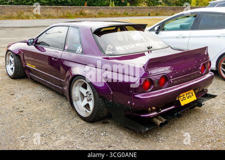 Violett modifizierter nissan Skyline R32 Sportwagen mit breiten Rädern und individuellem Spoiler auf einem Parkplatz, auf dem Änderungen an der Automobilindustrie gezeigt werden Stockfoto