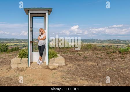 Eine Frau spricht am Telefon in einer Telefonzelle in einer abgelegenen ländlichen Gegend, Santo Pietro Belvedere, Italien Stockfoto
