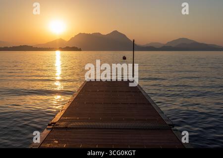Sonnenaufgang über dem Lago Maggiore Baveno mit Holzterrasse, die zum Wasser führt, Italien. Stockfoto