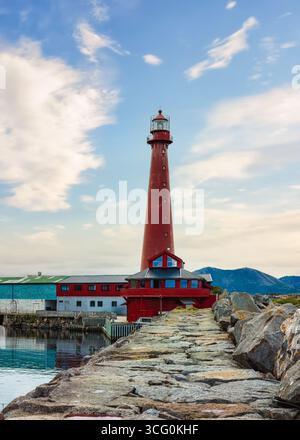 Der Leuchtturm des alten Andenes steht hoch auf einem felsigen Pier mit ruhigem Wasser, das den Himmel und die fernen Berge reflektiert und Küstenarchitektur und Natur zeigt Stockfoto