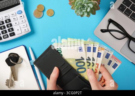 Hände, die Euro-Banknoten im Geldbeutel mit Taschenrechner, Münzen, Laptop und Brille halten. Persönliche Finanzen und Geldmanagement. Stockfoto