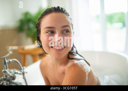 Entspannte junge Frau genießt Selbstpflege und Haarwäsche in der Badewanne. Stockfoto