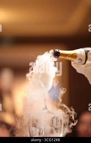 Barkeeper gießt Champagner in Glas, Nahaufnahme, Champagner fließt in ein Glas mit weißem Rauch Stockfoto