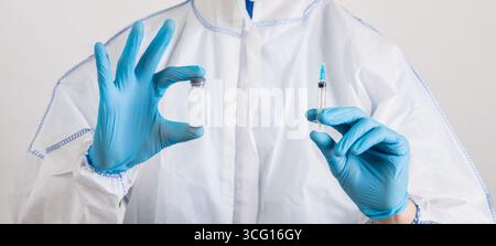 Medizinische Arbeiter in Gefahrgut Anzug, Maske und Gummihandschuhe halten covid-19-Impfstoff und Spritze auf hellem Hintergrund Stockfoto