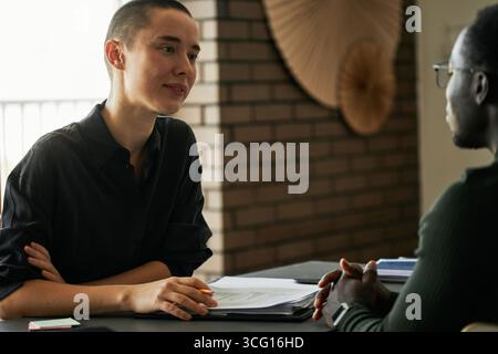Junger kaukasischer HR-Manager mit kurzen Haaren, der in einem modernen Büro arbeitet und den jungen Schwarzen Mann interviewt Stockfoto