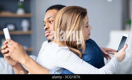 Gadget-Sucht-Konzept. Schwarzer Mann Und Weiße Frau, Die Smartphones Benutzen, Während Sie Sich Umarmen Stockfoto