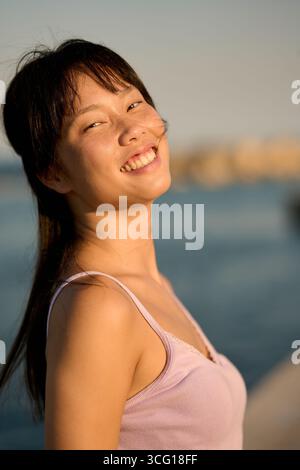 Junge Frau lächelt am Meer bei Sonnenuntergang Stockfoto