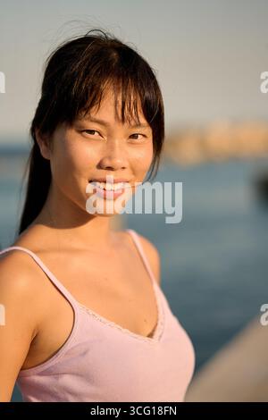 Junge asiatische Frau lächelt am Meer bei Sonnenuntergang Stockfoto