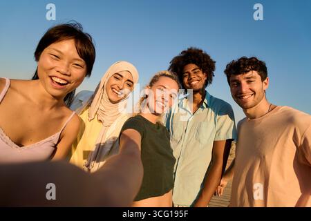 Glückliche, ethnische Freunde machen Selfie bei Sonnenuntergang und genießen den Sommerurlaub Stockfoto