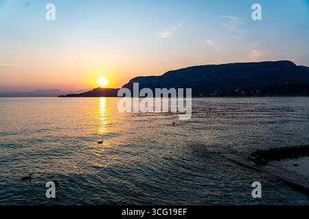 Sonnenuntergang über dem Gardasee mit Enten auf dem Wasser und Bergsilhouette, Italien Stockfoto