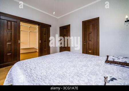 Ein Schlafzimmer mit einem weißen Bett und zwei Kissen. Das Bett ist mit einer Decke mit Blumenmuster bedeckt Stockfoto