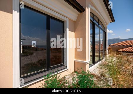 Das Haus hat große Fenster, die schwarz und klar sind. Die Fenster befinden sich an der Seite des Gebäudes und sind weiß eingerahmt. Das Haus befindet sich auf einer h Stockfoto