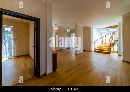 Ein großes offenes Wohnzimmer mit einer Treppe, die in den zweiten Stock führt. Das Zimmer ist leer und hat ein sauberes, modernes Aussehen Stockfoto