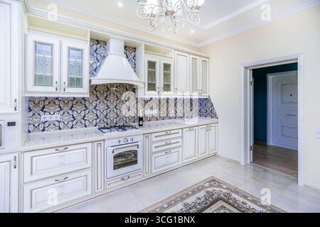 Eine Küche mit weißen Schränken und einer blau-goldenen Wand. Die Theke ist weiß und das Waschbecken weiß Stockfoto