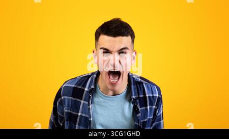 Frustrierter junger Mann, der vor Wut schreit und seine Wut über orangen Studiohintergrund ausdrückt. Konzept der negativen Emotionen Stockfoto