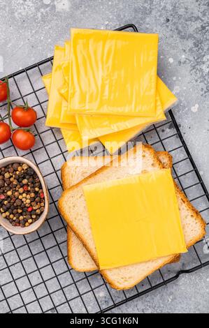 Quadratische Scheiben von verarbeitetem Cheddar-Käse in Einzelverpackung aus Kunststoff. Grauer Hintergrund. Draufsicht. Stockfoto