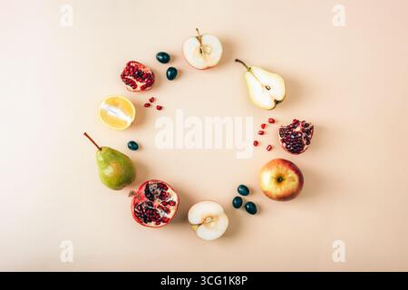 Flache Komposition mit Kreis aus frischen Früchten einschließlich Apfel, Birne, Granatapfel, Zitrone und Trauben auf pastellbeigem Hintergrund mit Kopierraum. Stockfoto