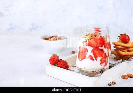 Gesundes Frühstück mit Zutaten. Erdbeerjoghurt mit Beeren, französischer Cracker und Müsli auf einem hellen Tisch, Obstsalat, Detox Diät und natürlich Stockfoto