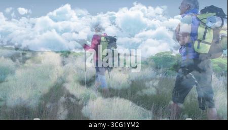 Wanderer mit Jacken über das Feld unter bewölktem Himmel, Stöcke und Rucksäcke mit Pads Stockfoto