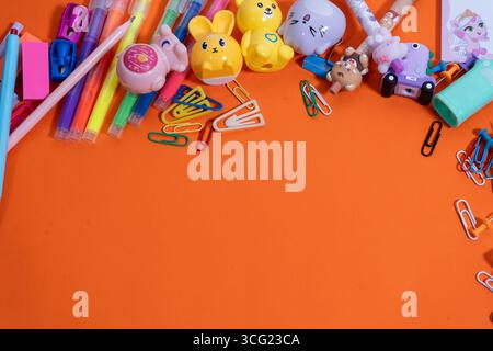Flache Komposition aus farbenfrohen Schulutensilien, die einen Rahmen auf orangefarbenem Hintergrund bilden, perfekt für Werbeaktionen im Schulbereich Stockfoto