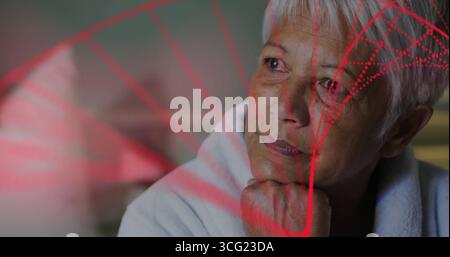 Eine Seniorin im Bademantel, die im Schlafzimmer blickt, mit roten geometrischen Projektionsmustern Stockfoto
