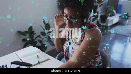 Frau, die im Home Office Kopfhörer mit schwebenden digitalen Symbolen und Kopierraum auf einem Laptop einstellt Stockfoto