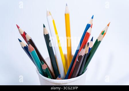 Bunte Bleistifte stehen aufrecht in einem weißen Papierbecher, bereit zum Zeichnen und Färben Stockfoto