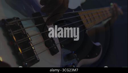 Die Hand des Musikers zupfen, um weiße E-Bass-Saiten auf der dunklen Bühne mit farbigen Lichtern zu erkunden Stockfoto