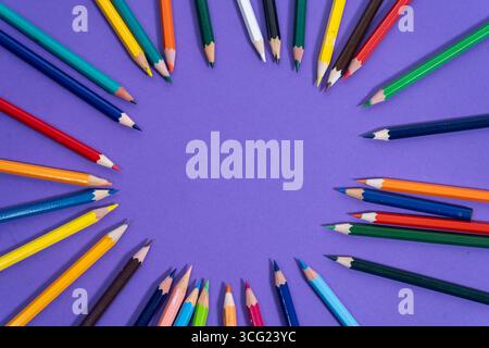 Farbenfrohe Bleistifte, die in einem Kreis auf einer lila Oberfläche angeordnet sind, schaffen einen lebendigen und künstlerischen Rahmen mit leerem Raum in der Mitte Stockfoto