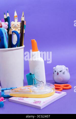 Schreibwaren-Set mit Bleistiften, Scheren, Kleber, Korrekturband und anderen Gegenständen auf einem violetten Hintergrund, um einen lebendigen und verspielten Rücken zu schaffen Stockfoto