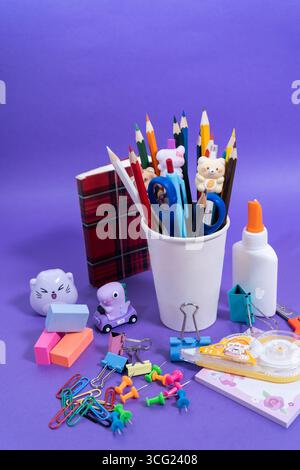 Bunte Bleistifte, Radierer, Leim, Scheren und andere Schreibwaren sind ordentlich auf einer lila Oberfläche angeordnet, perfekt für Schulprojekte Stockfoto