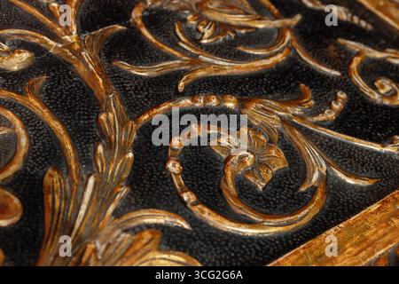 Detailgetreue goldene Blumenmuster auf einer schwarzen strukturierten Oberfläche, die elegante Handwerkskunst und dekorative Kunst in einem Vintage-Look zeigen Stockfoto
